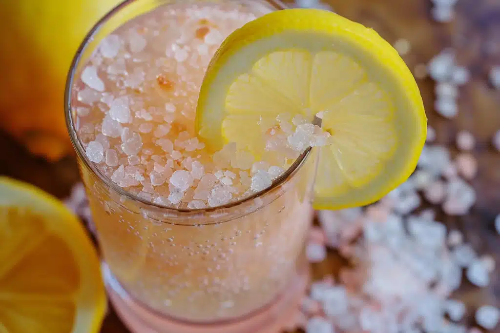Glass of pink Himalayan salt water with lemon slice — part of the pink salt trick for weight loss morning drink.